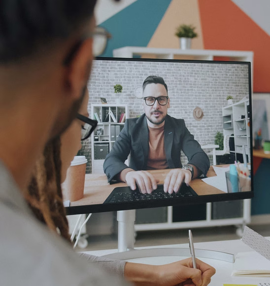 Someone taking notes during a video call with a collaborator on a desktop monitor
